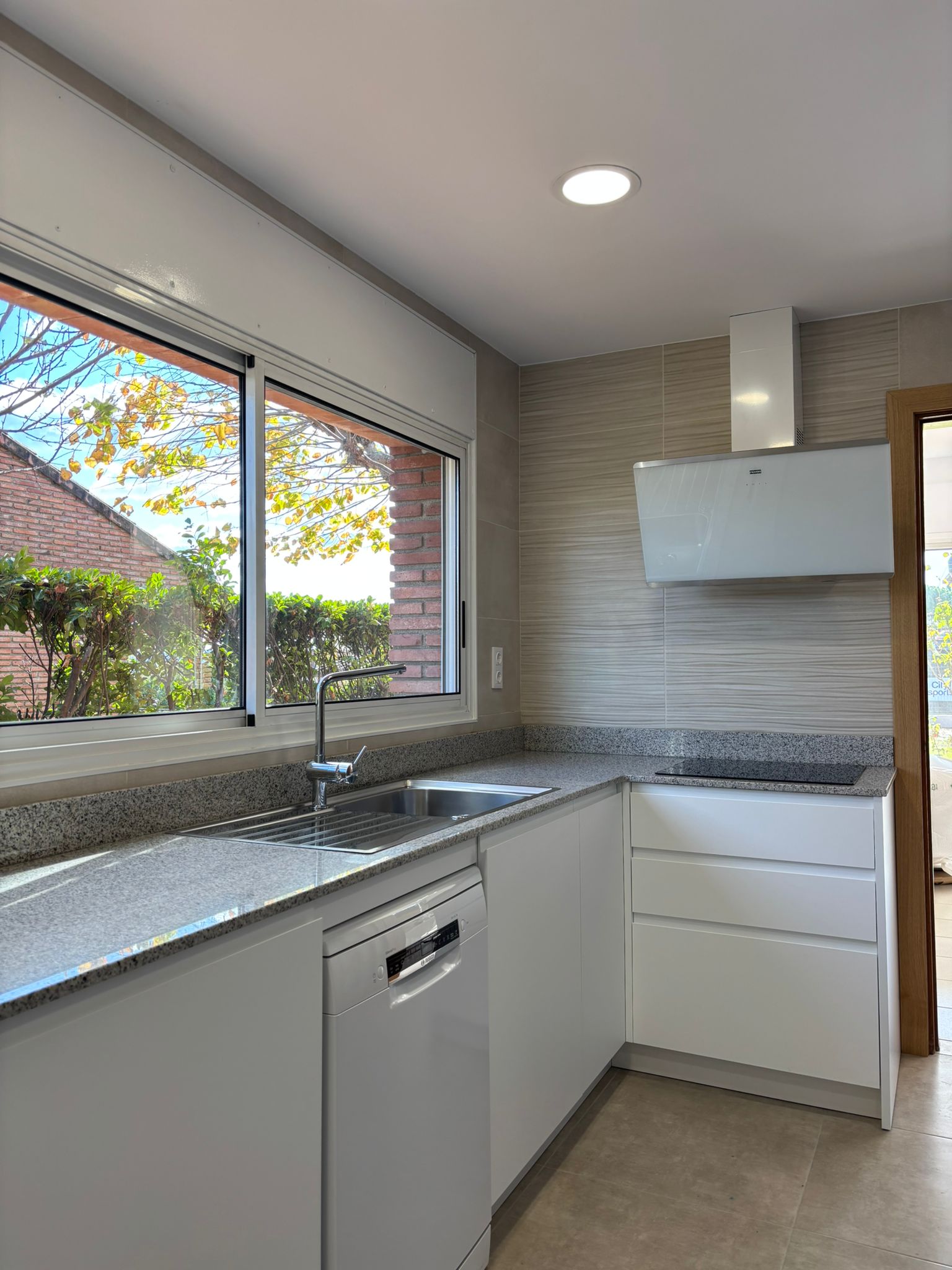 Cocina reformada con placa vitrocerámica, campana blanca y alicatado claro.